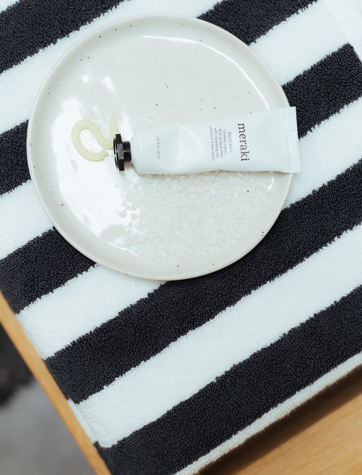 een detail shot van een zwart met wit gestreepte handdoek en daar bovenop een schaaltje met handcrème 