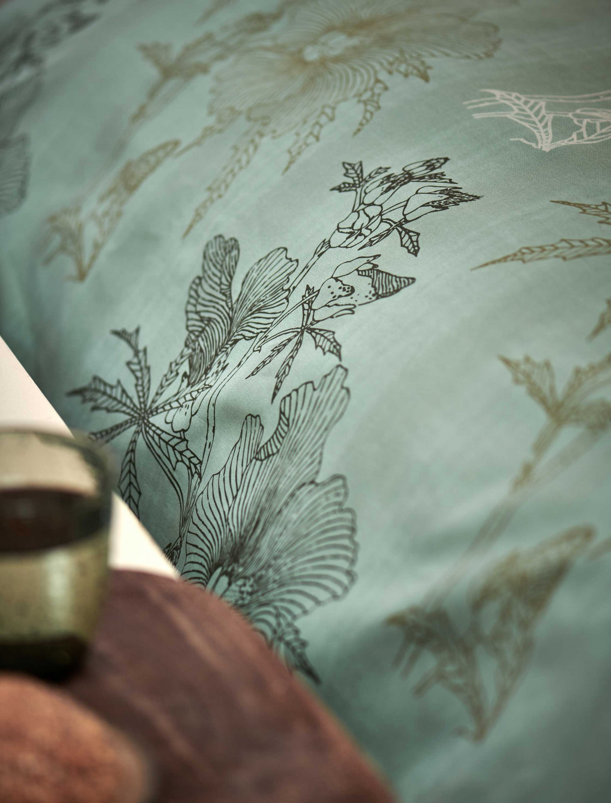 detail shot van een dekbedovertrek in een groene kleur met een print van bladeren en bloemen