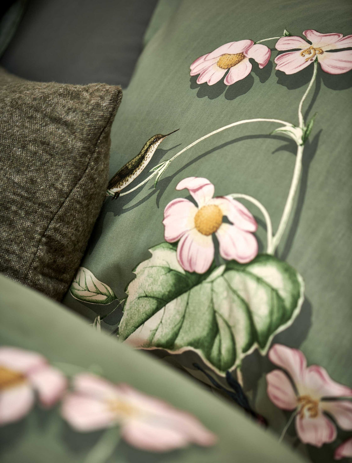 detail shot van een hoofdkussen in een groene kleur met een print van vogels en bloemen