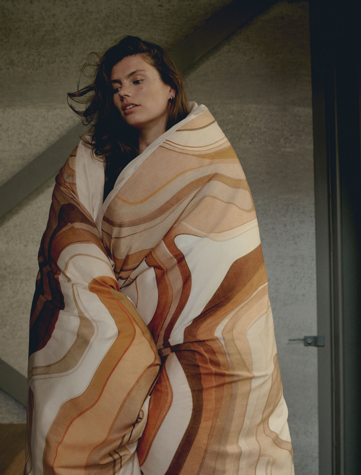 Een vrouw met een dekbedovertrek om haar heen geslagen in een print met bruine en oranje kleuren