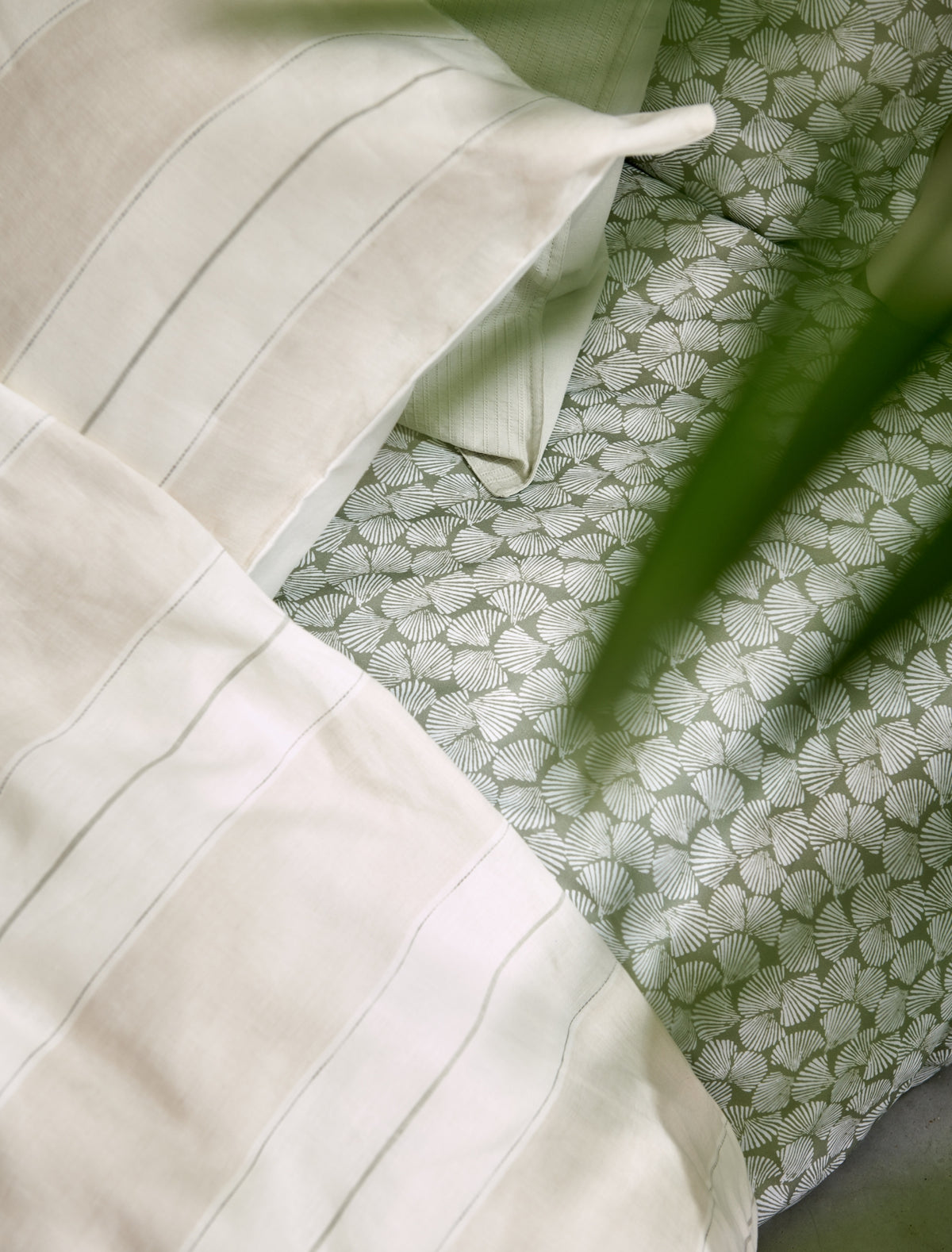 detail shot van een dekbedovertrek in beige met strepen en een dekbedovertrek met schelpen op een groene achtergrond