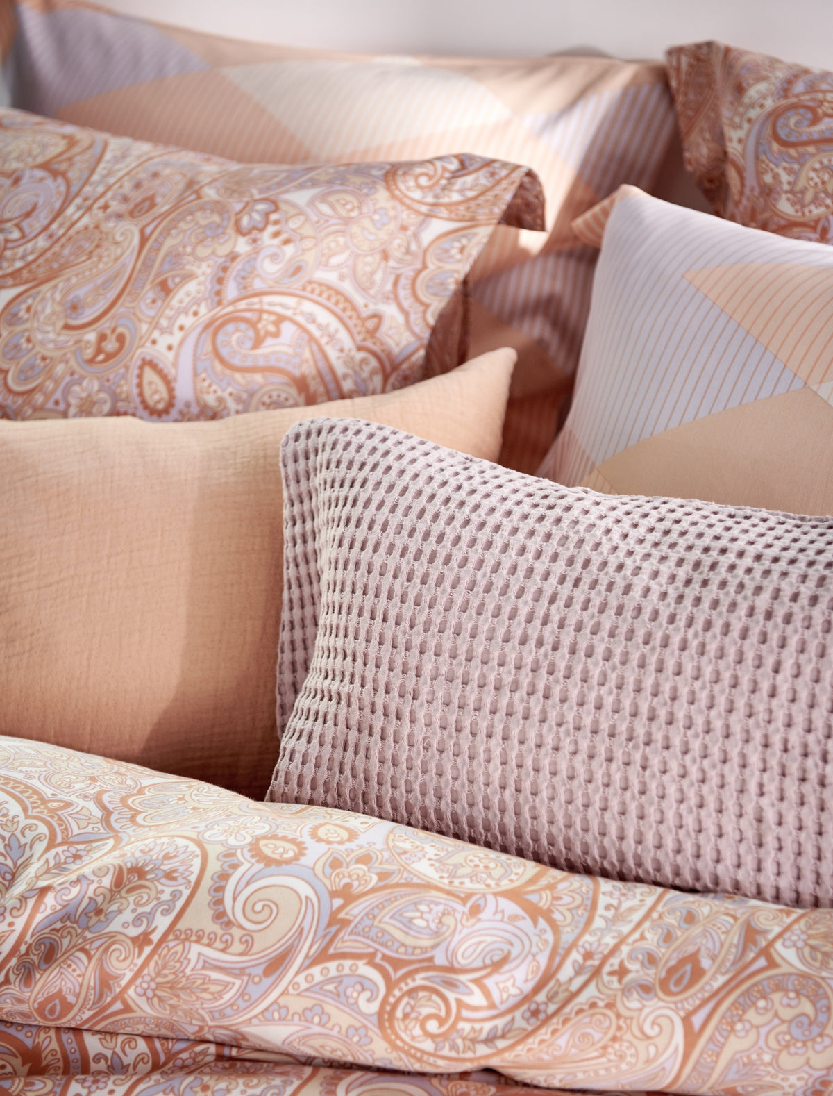detail shot van een bed met kussens in oranje en lila pastel kleuren 