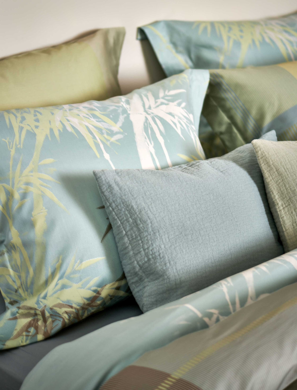 Palm Paradise thyme dekbedovertrek heeft silhouetten van palmbomen in bruin, beige, groen en wit op een lichtblauwe achtergrond. De achterkant van het dekbedovertrek heeft dezelfde print. De kussens hebben aan beide kanten palmbomen.