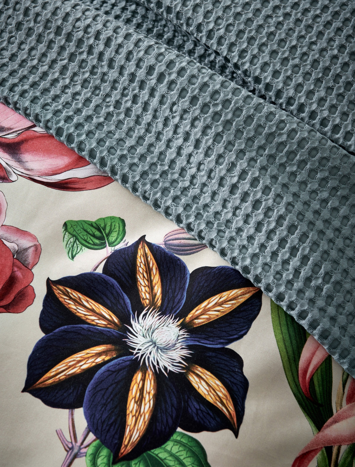 detail shot van een plaid met waffle structuur in een blauwe kleur en een dekbedovertrek met bloemen en een beige ondergrondkleur
