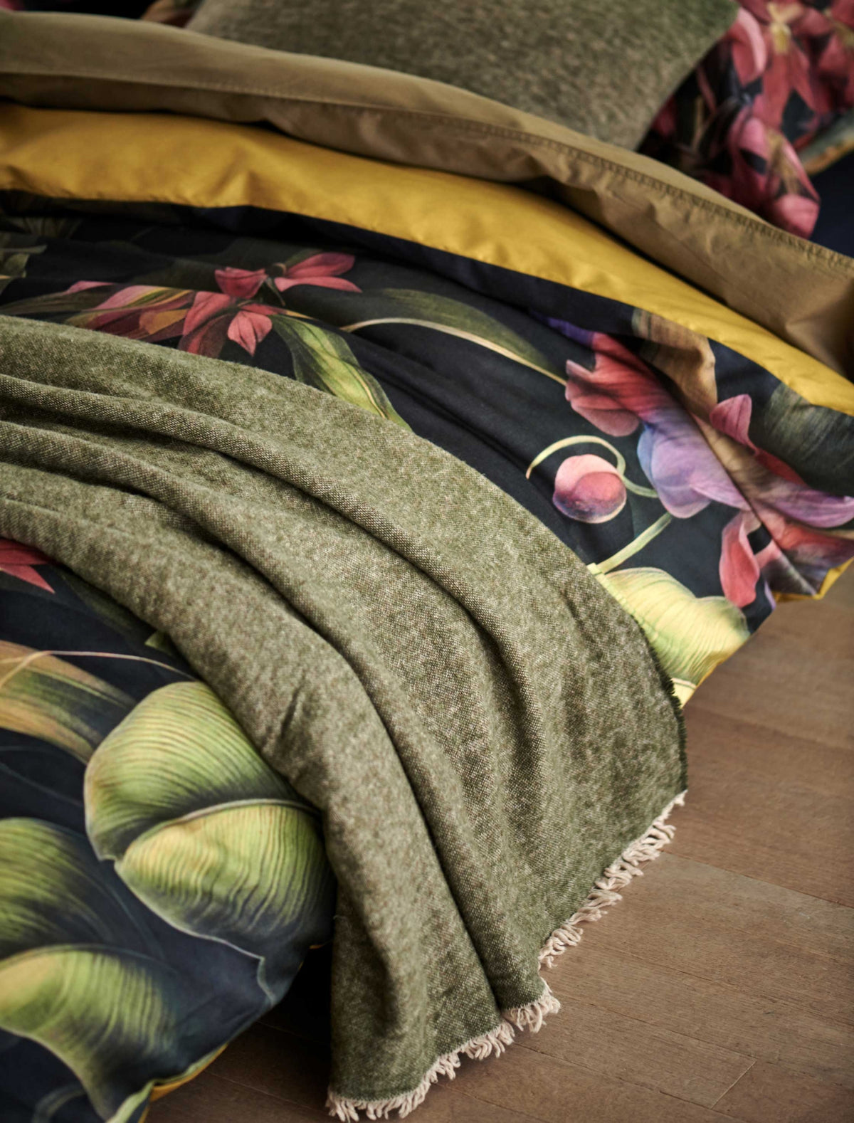 detail shot van een bed met een overtrek met bloemen en planten en een wollen plaid in groen