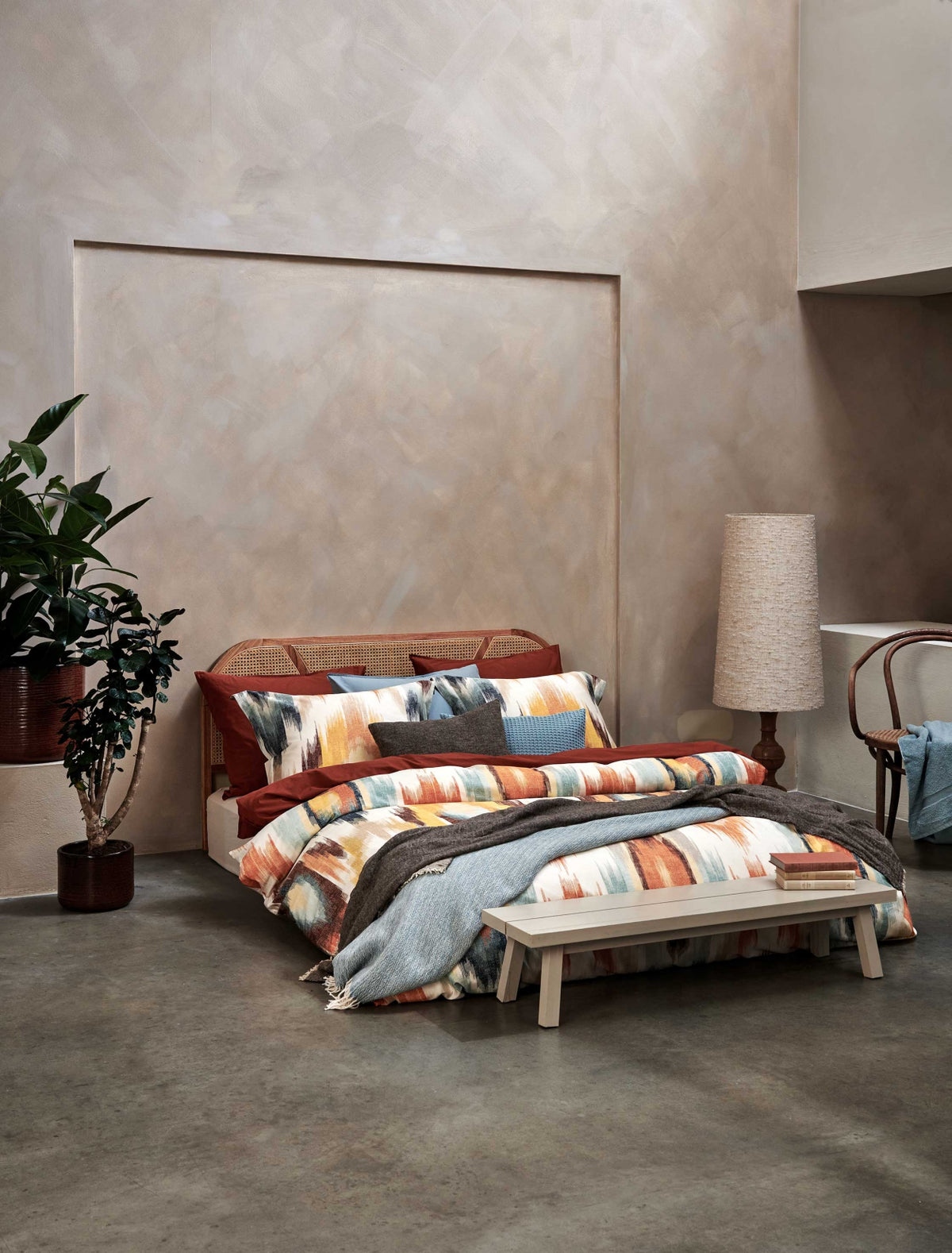 een bed in een rustige omgeving  met een dekbedovertrek met print in oranje en blauwe kleuren 