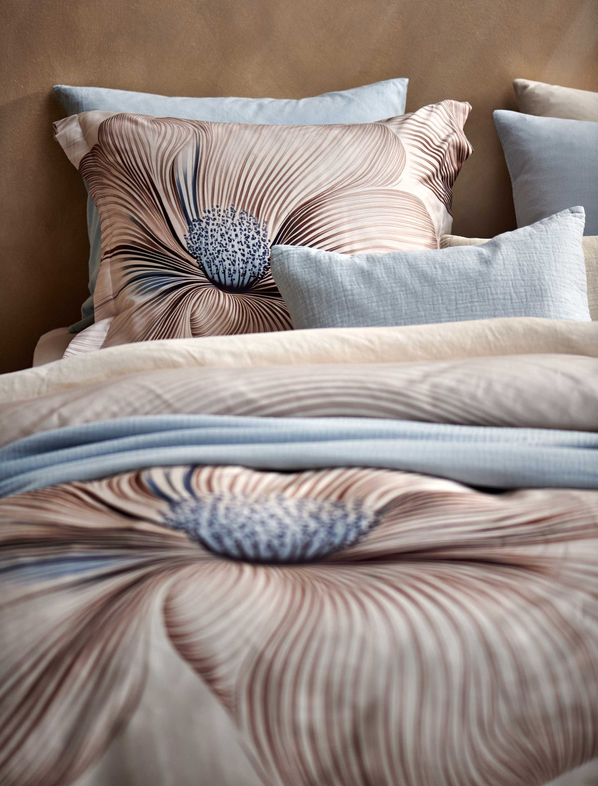 detail shot van een bed met een beige dekbedovertrek met een grote bloem als print in bruine en lichtblauwe kleuren