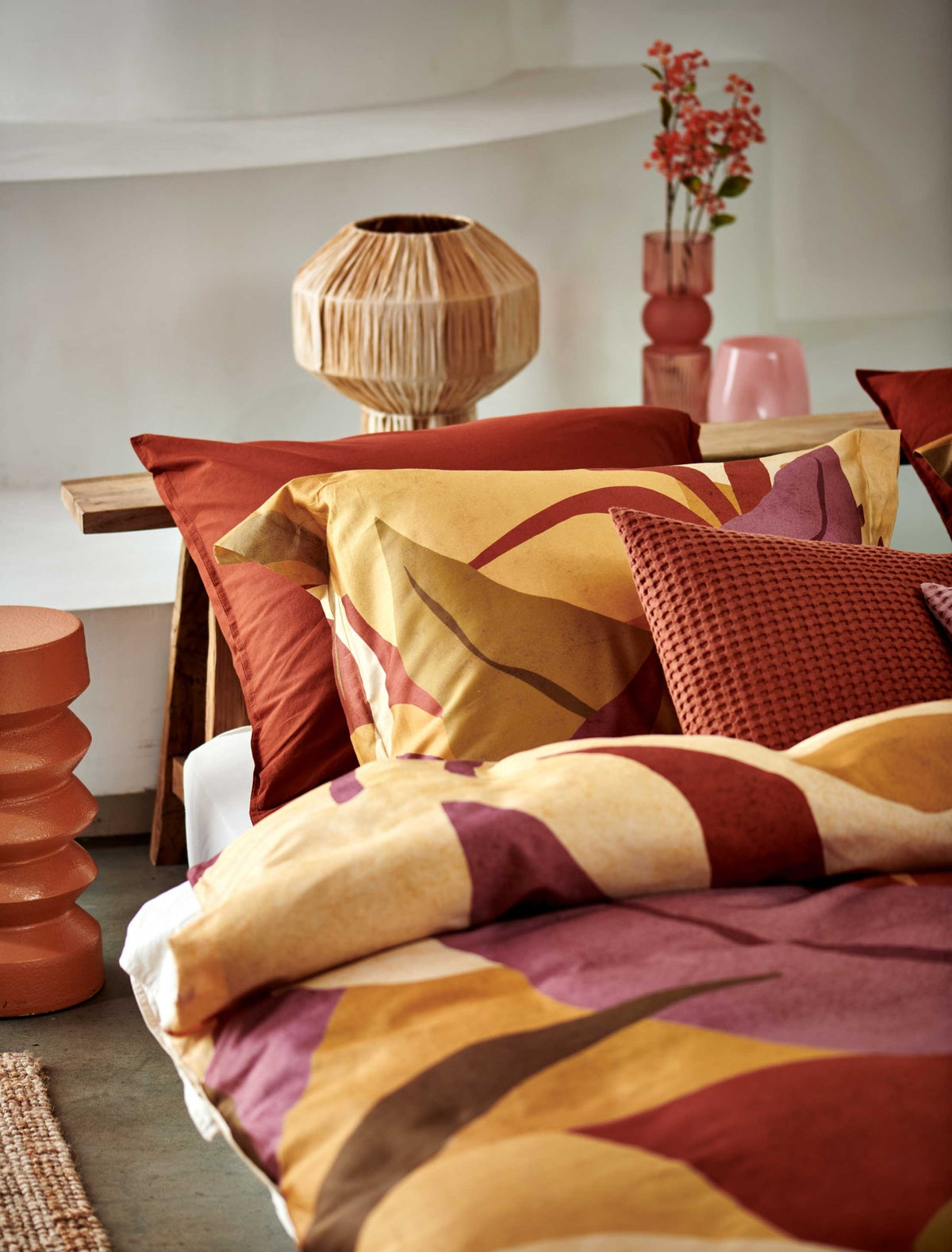 detail shot van een bed met een dekbedovertrek in warme gele, roze en groene kleuren en een dekbedovertrek een warme rusty brown kleur