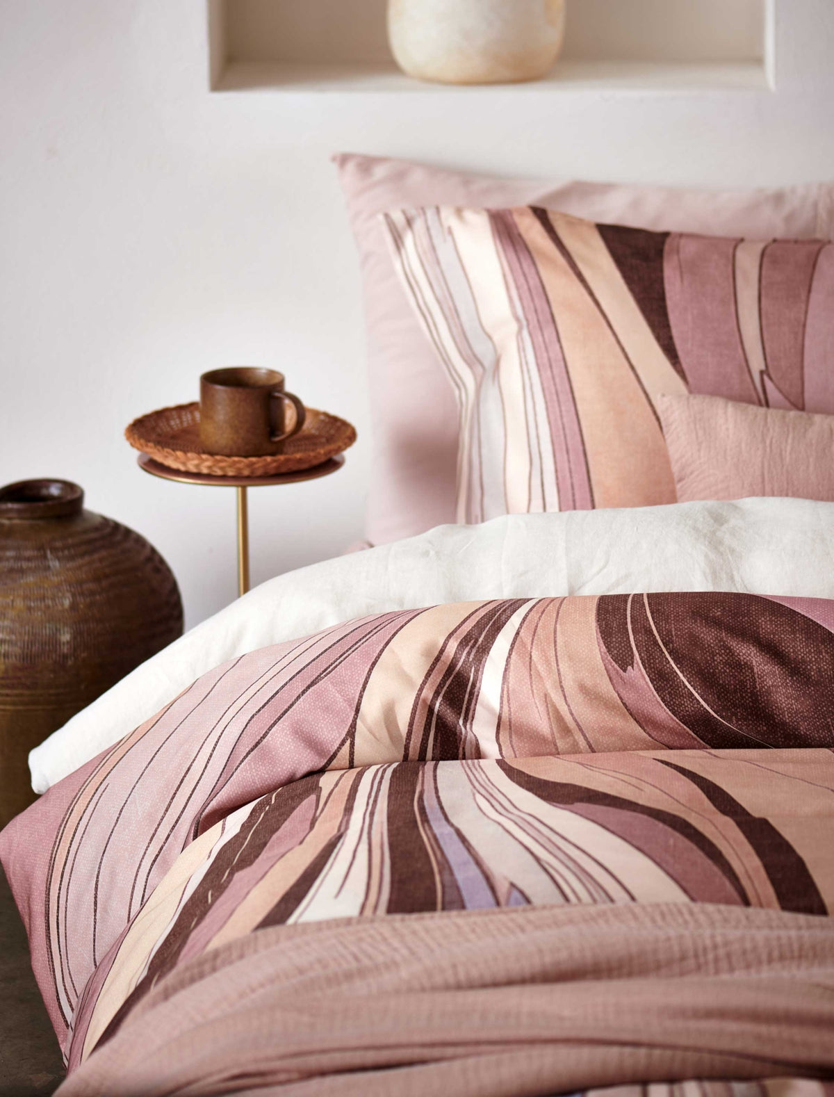 Swirls moonscape dekbedovertrek heeft een abstracte versie van een marmerpatroon met paars, roze en bruine tinten. De achterkant van het dekbedovertrek is effen offwhite. De kussens hebben aan beide zijden hetzelfde patroon. 