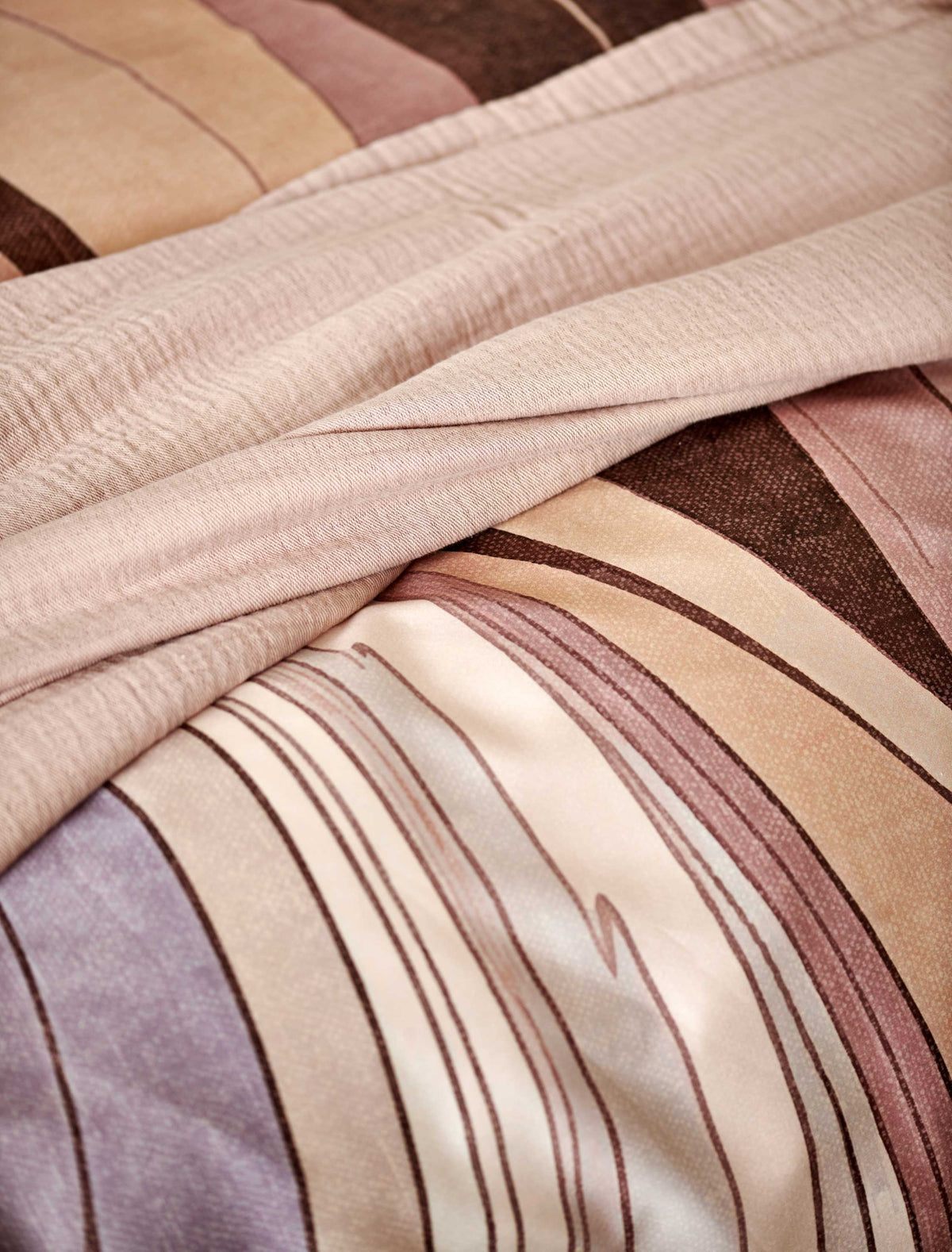 Swirls moonscape dekbedovertrek heeft een abstracte versie van een marmerpatroon met paars, roze en bruine tinten. De achterkant van het dekbedovertrek is effen offwhite. De kussens hebben aan beide zijden hetzelfde patroon. 