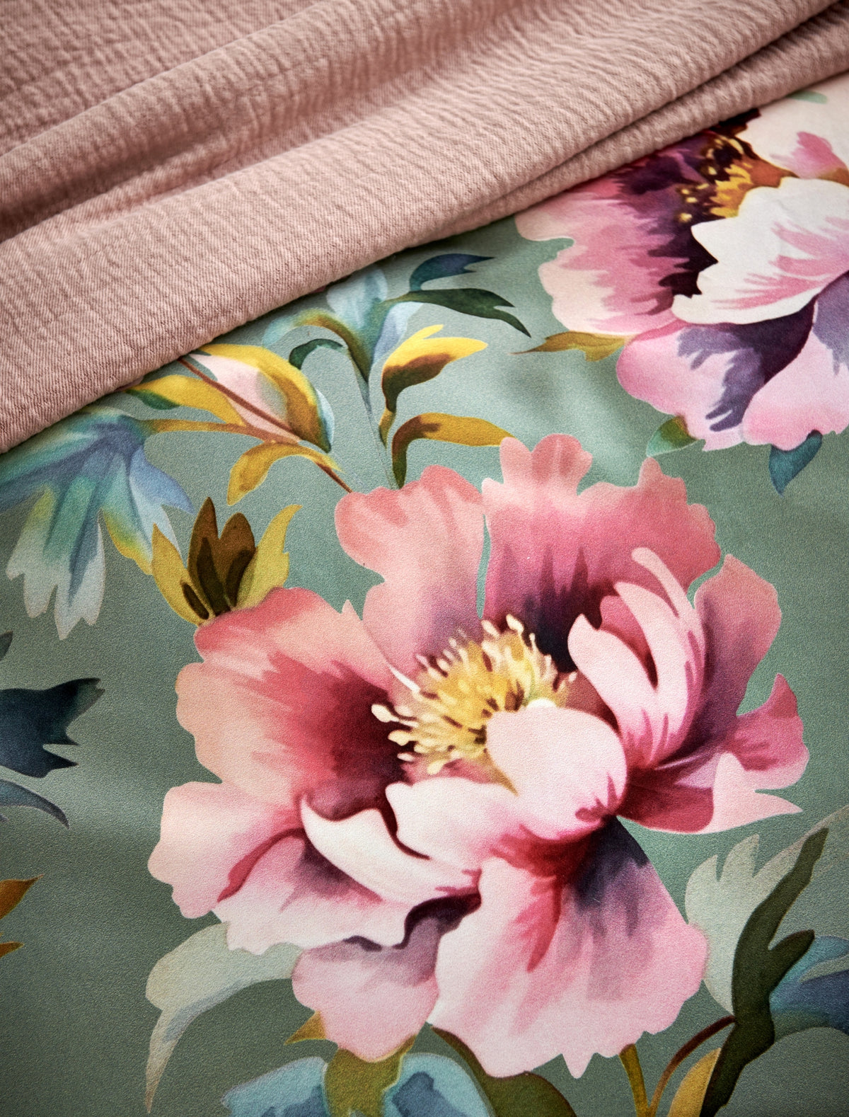 detail shot van een dekbedovertrek met roze bloemen op een groene achtergrond en een plaid in een blush kleur