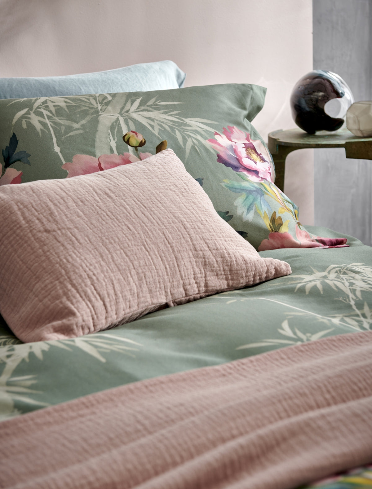detail shot van een bed met een dekbedovertrek in een groene kleur met roze bloemen en bamboe takken en een roze kussen