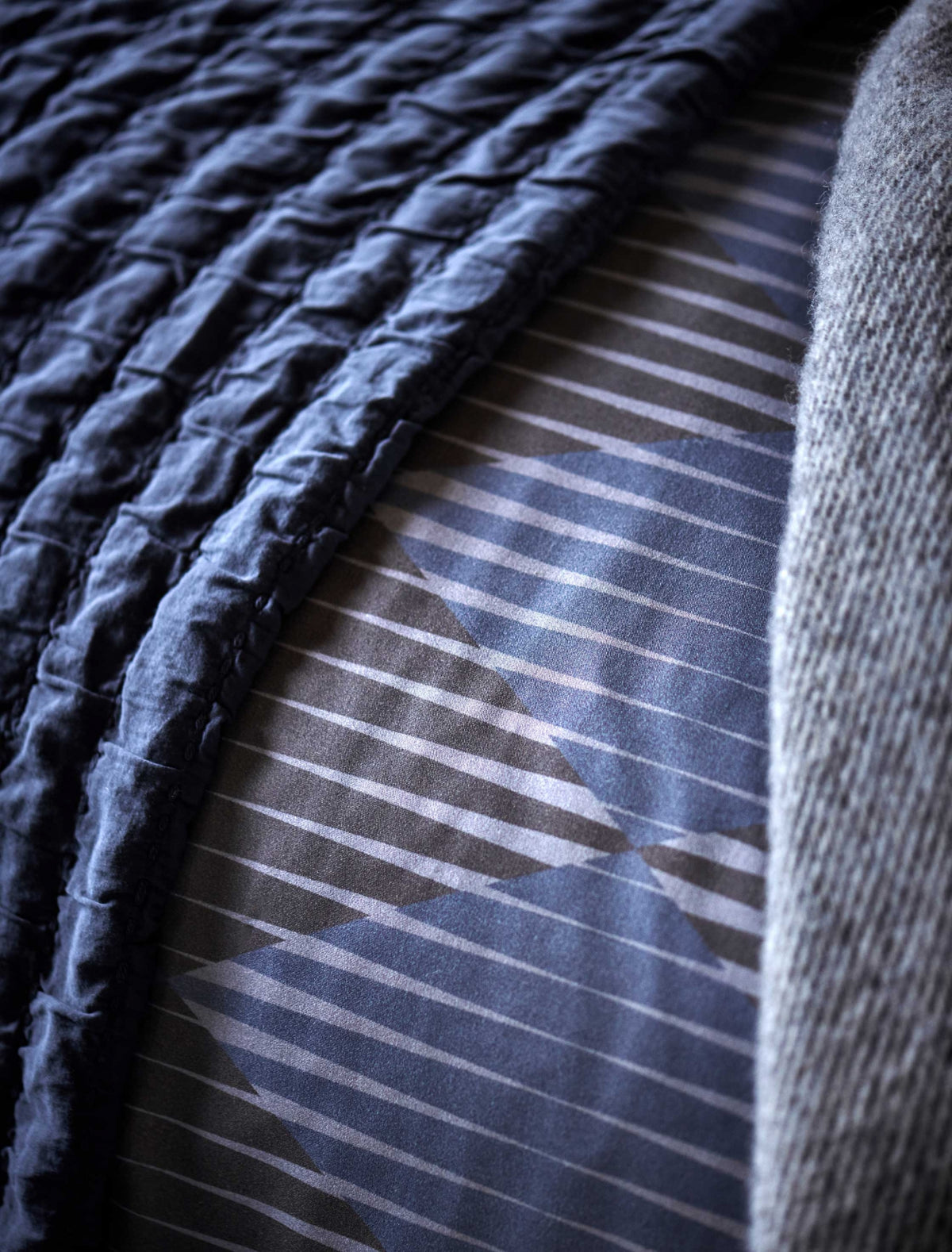 detail shot van een dekbedovertrek met grafische print in grijze en donkerblauwe kleuren en een plaid in een donkerblauwe kleur