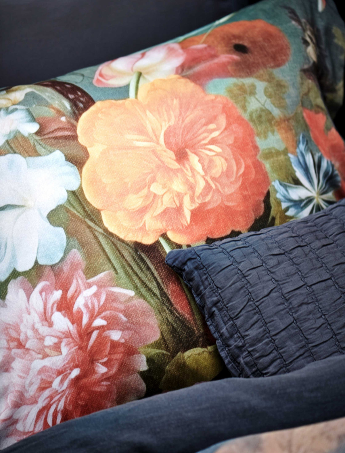 detail shot van een hoofdkussen met een bloemenprint in oranje en roze tinten en een sierkussensloop in het blauw