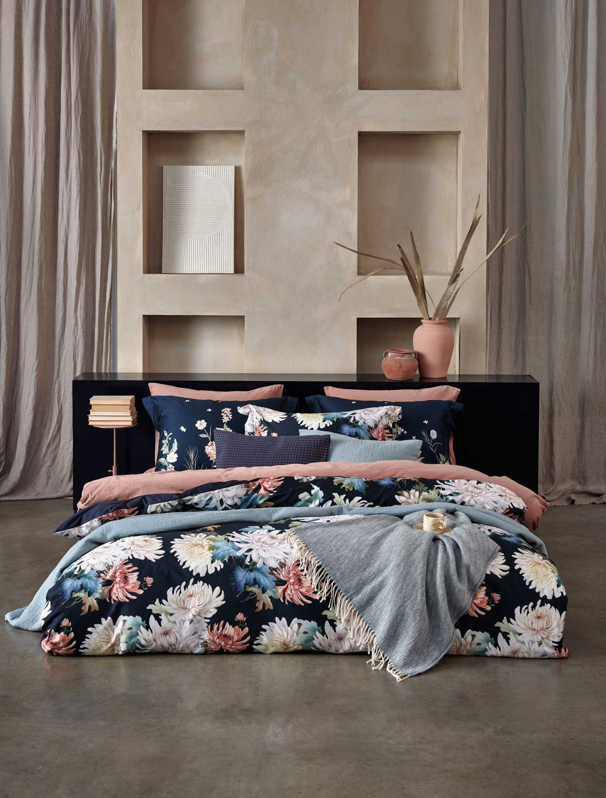 Floral Bliss blue ink dekbedovertrek heeft roze, oranje en rode bloemen met herstbladeren er omheen op een donkerblauwe achtergrond. De achterkant van het dekbedovertrek is effen donkerblauw. De kussens hebben hebben aan beide zijden dezelfde bloemen. 