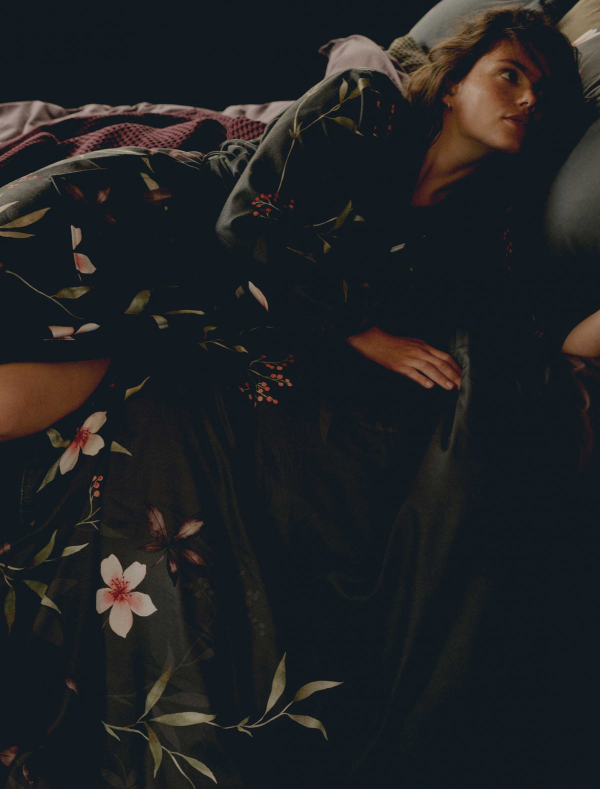 Een vrouw die op een bed ligt met een badjas aan met bloemen in een off black kleur