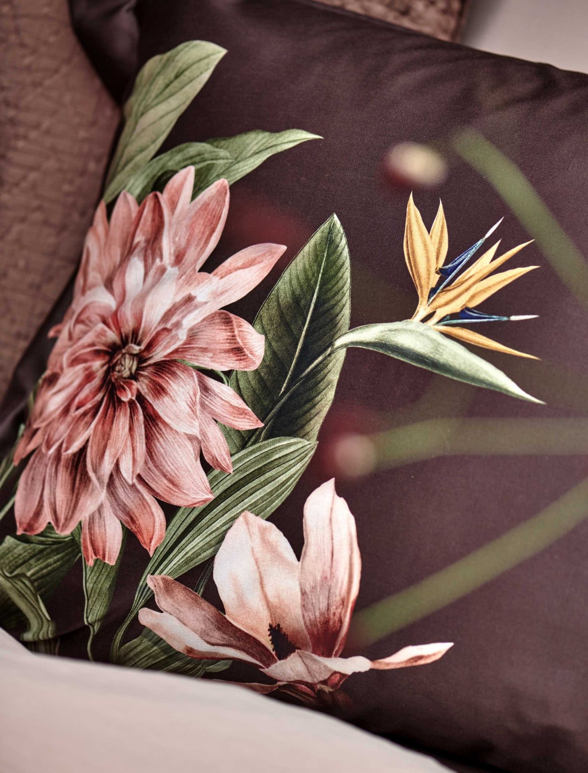 detail shot van een bruin hoofdkussen met een roze bloem en groene bladeren en een paradijsvogel