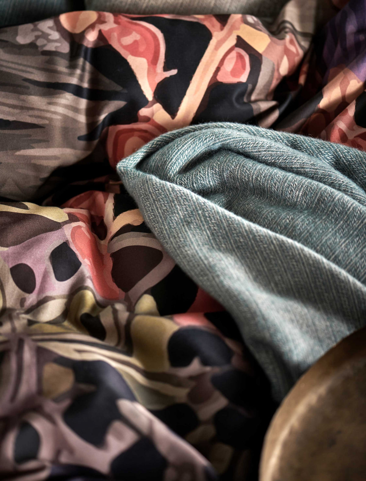 detail shot van een plaid van wol mix in een blauwe kleur en een dekbedovertrek met print in paarse en oranje kleuren
