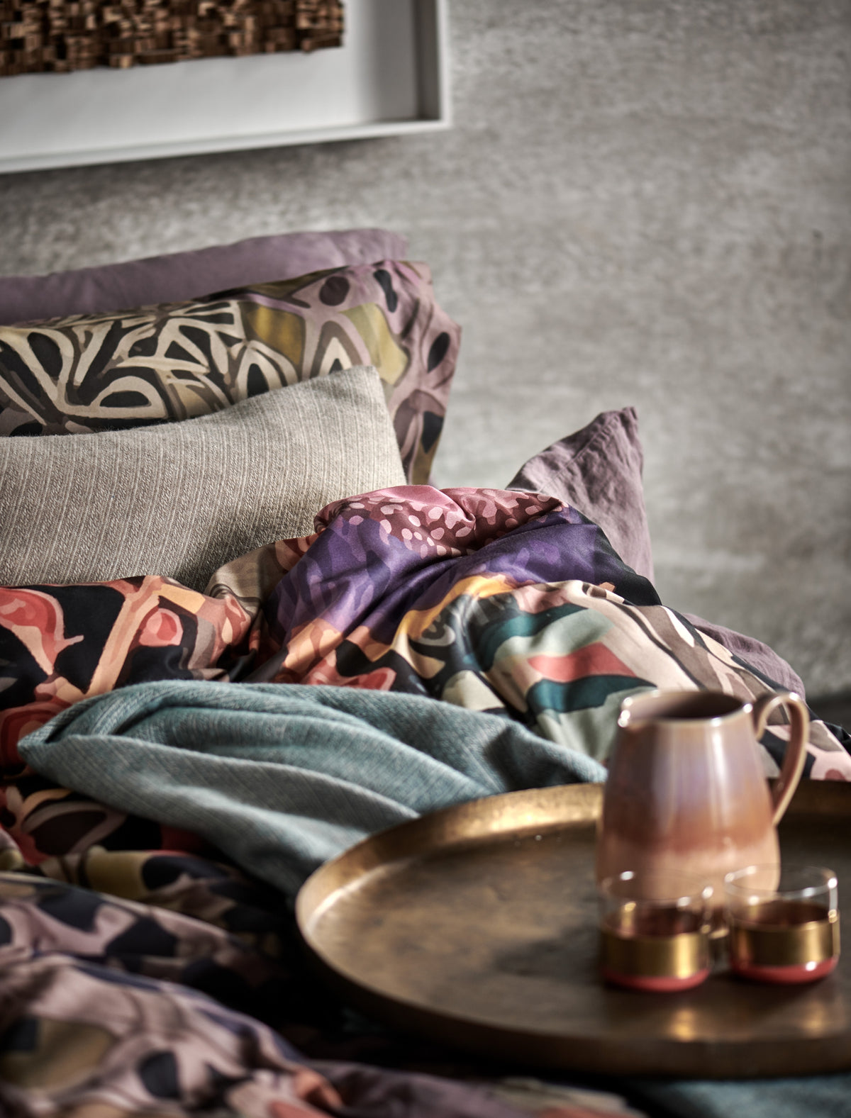 detail shot van een bed met een dekbedovertrek met print en een sierkussen in een beige kleur en een koffiekan met twee kopjes