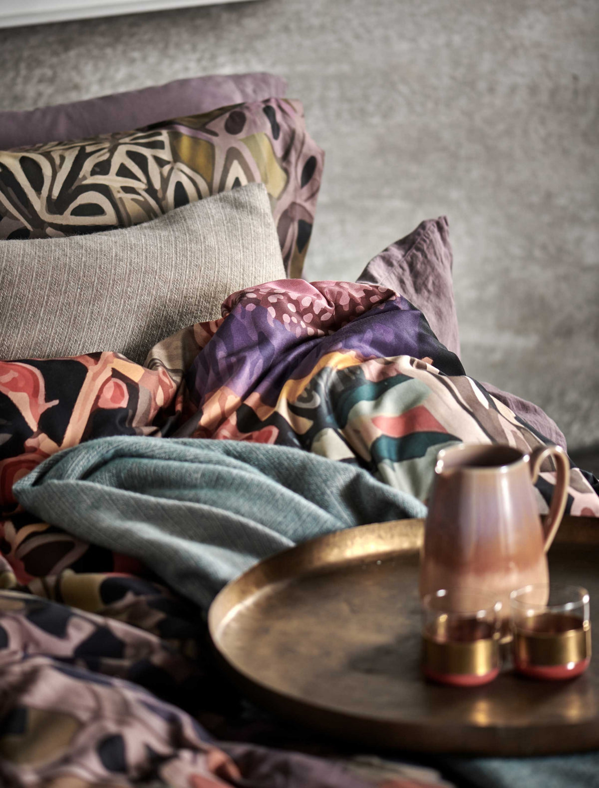 detail shot van een bed met een dekbedovertrek met print en een sierkussen in een beige kleur en een koffiekan met twee kopjes