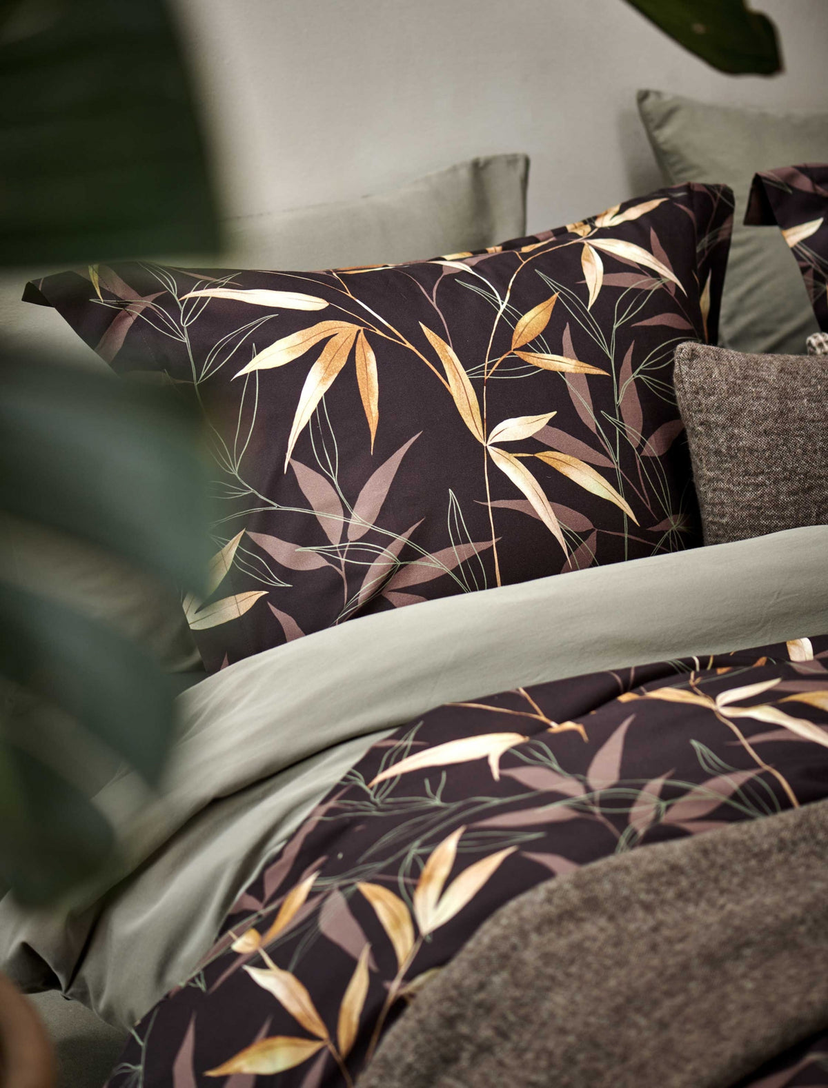 detail shot van een bed met een bruin dekbedovertrek met bamboe takken en een groen/thyme dekbedovertrek 