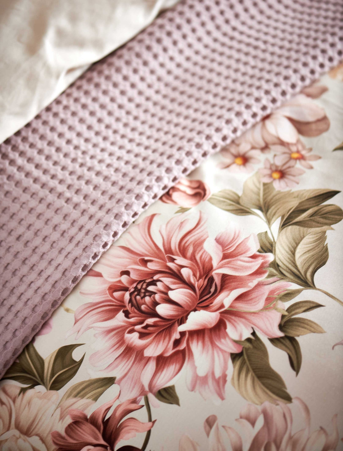 detail shot van een dekbedovertrek in een beige kleur met roze bloemen en een wafelsprei in een lila kleur