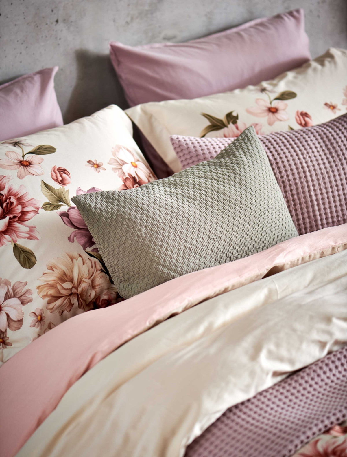 detail shot van een bed met een beige dekbedovertrek met roze en beige bloemen en sierkussens in lila en groene kleuren