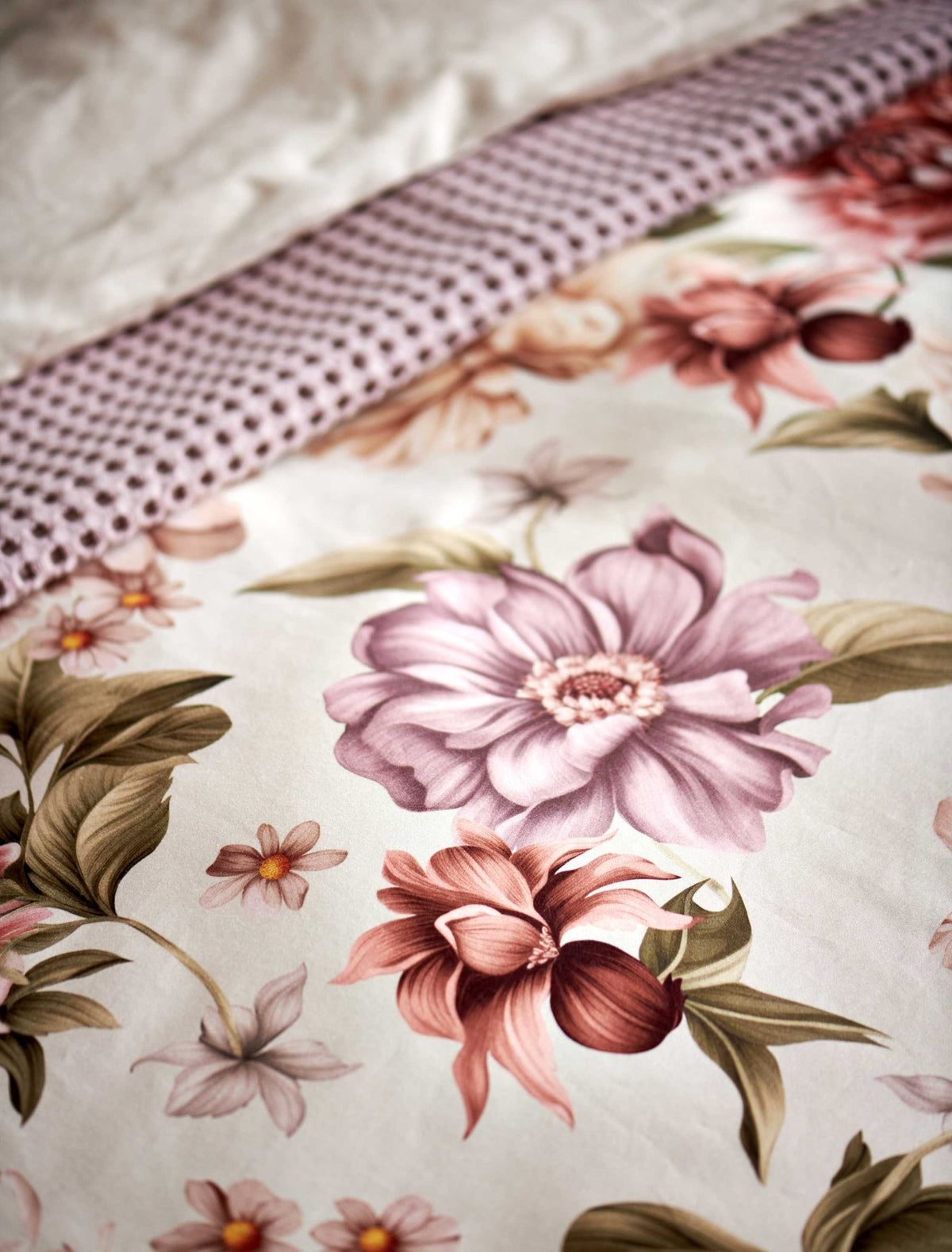 detail shot van een dekbedovertrek in een beige kleur met roze en paarse bloemen met groene bladeren