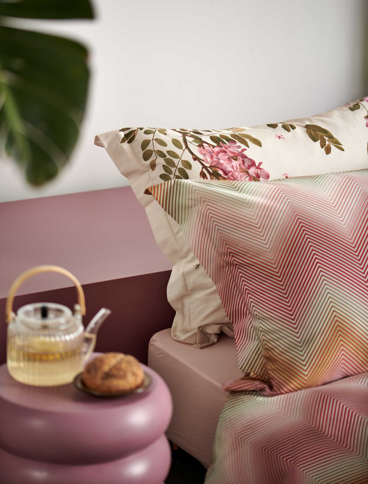 detail shot van een hoofdkussen met zigzag print in roze, groen en oranje kleuren en een hoofdkussen met roze bloemen en groene bladeren